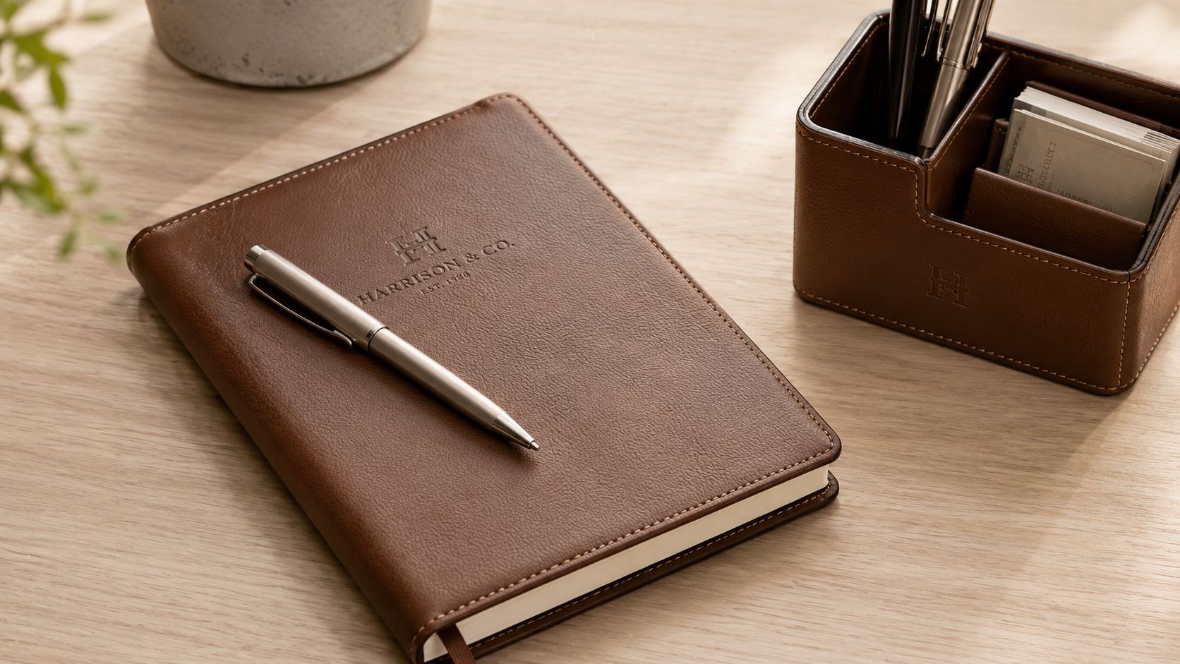 A leather-bound journal and a pen set with a matching desk organizer on a wooden surface.